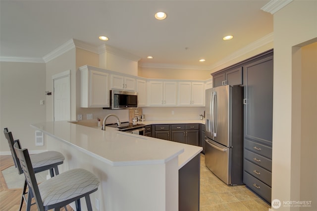 kitchen with ornamental molding, a kitchen breakfast bar, a peninsula, appliances with stainless steel finishes, and light countertops