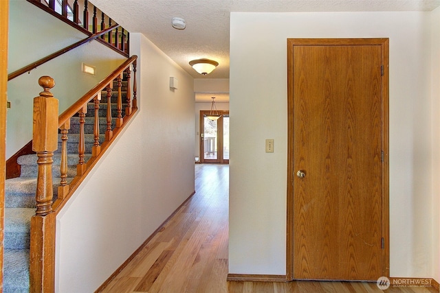 hallway with a textured ceiling, stairway, light wood-style flooring, and baseboards