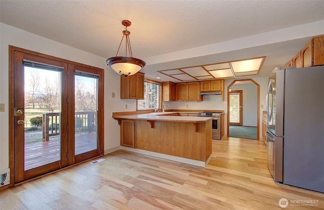 kitchen with a breakfast bar, decorative light fixtures, stainless steel appliances, light countertops, and a peninsula