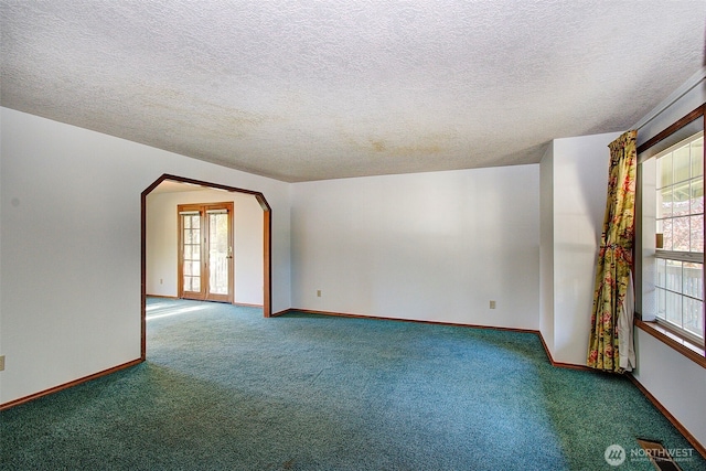 carpeted spare room with arched walkways, plenty of natural light, and baseboards