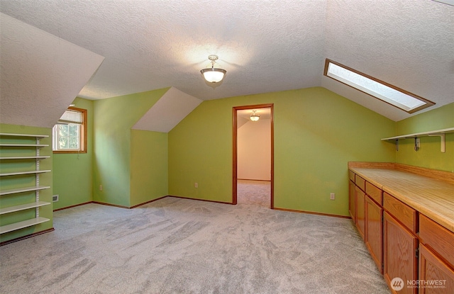 additional living space with light carpet, vaulted ceiling with skylight, baseboards, and a textured ceiling