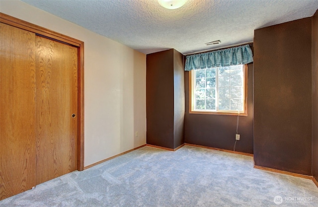 unfurnished bedroom with light carpet, baseboards, visible vents, a textured ceiling, and a closet