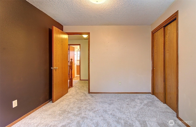 unfurnished bedroom featuring a textured ceiling, a closet, and light colored carpet