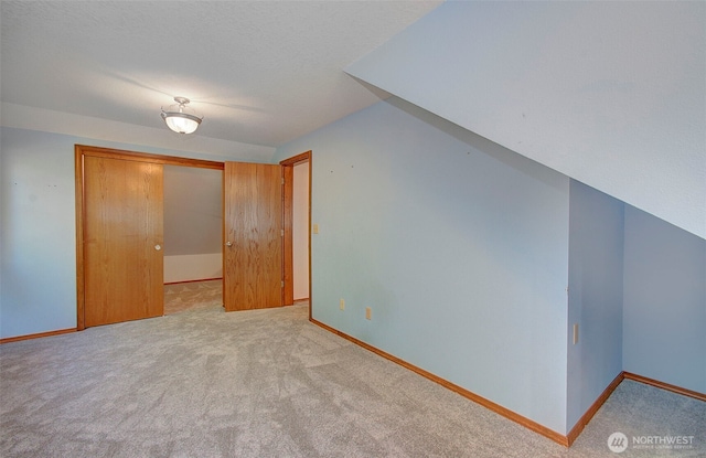 bonus room featuring light carpet, a textured ceiling, and baseboards