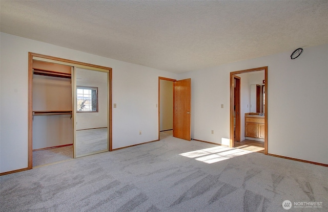 unfurnished bedroom featuring a textured ceiling, ensuite bathroom, light colored carpet, baseboards, and a closet