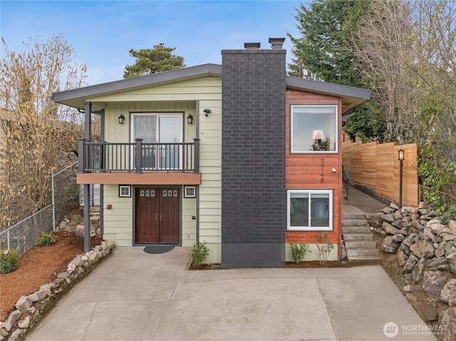 view of front facade with a balcony, a chimney, fence, and a patio