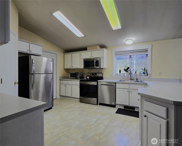 kitchen with stainless steel appliances, light countertops, white cabinetry, vaulted ceiling, and a sink