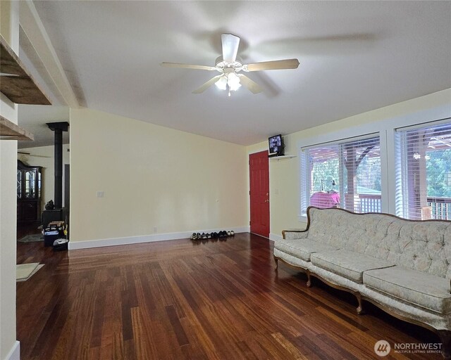 living room with a wood stove, ceiling fan, baseboards, and dark wood-type flooring