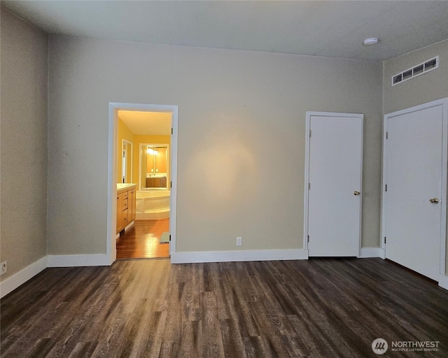 unfurnished bedroom featuring ensuite bath, baseboards, visible vents, and dark wood-type flooring