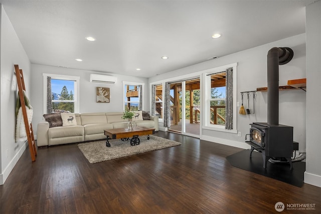 living area with plenty of natural light, an AC wall unit, a wood stove, and wood finished floors