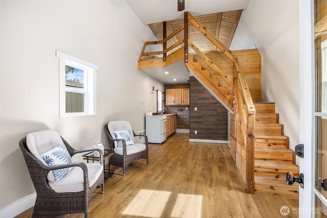 sitting room with baseboards, stairway, high vaulted ceiling, and light wood-style floors