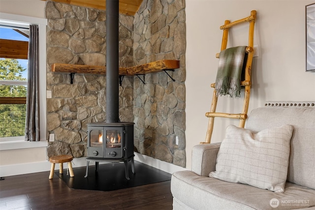 unfurnished living room featuring a wood stove, wood finished floors, and baseboards