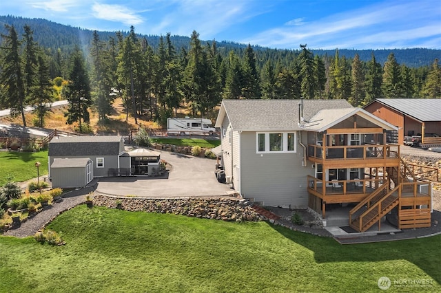 back of house featuring stairs, a forest view, a wooden deck, an outbuilding, and a lawn