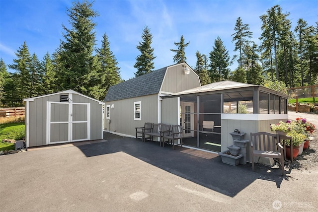 back of house with a patio, an outdoor structure, a gambrel roof, fence, and a shingled roof