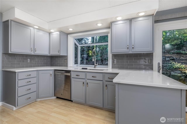 kitchen featuring a sink, stainless steel dishwasher, light wood finished floors, and gray cabinets