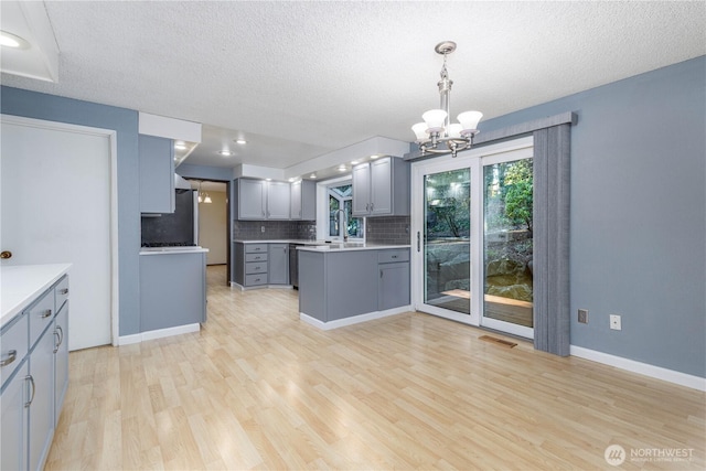 kitchen featuring light wood-style flooring, gray cabinetry, visible vents, light countertops, and pendant lighting