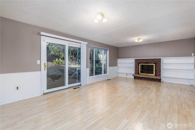 unfurnished living room featuring light wood finished floors, visible vents, a wainscoted wall, a textured ceiling, and a fireplace