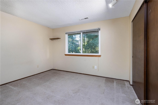 unfurnished bedroom featuring light carpet, a textured ceiling, visible vents, and baseboards