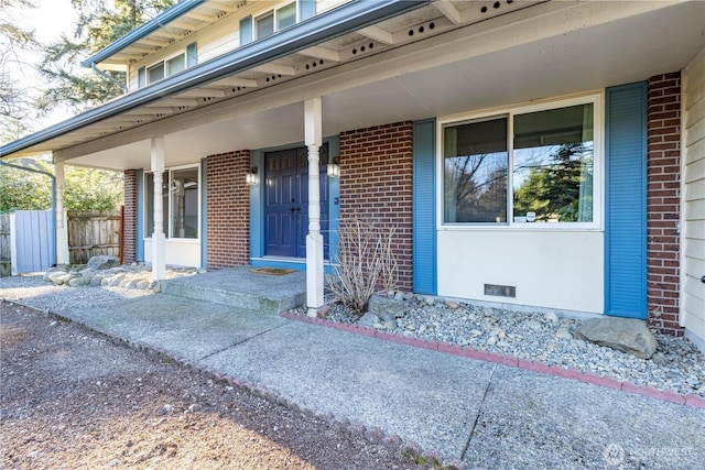 property entrance featuring visible vents, crawl space, covered porch, fence, and brick siding