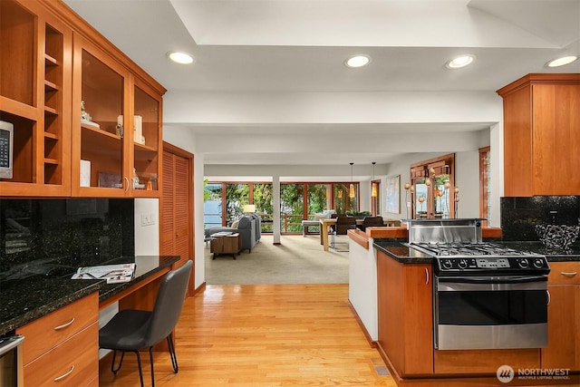 kitchen with glass insert cabinets, dark stone counters, stainless steel range with gas stovetop, and built in desk