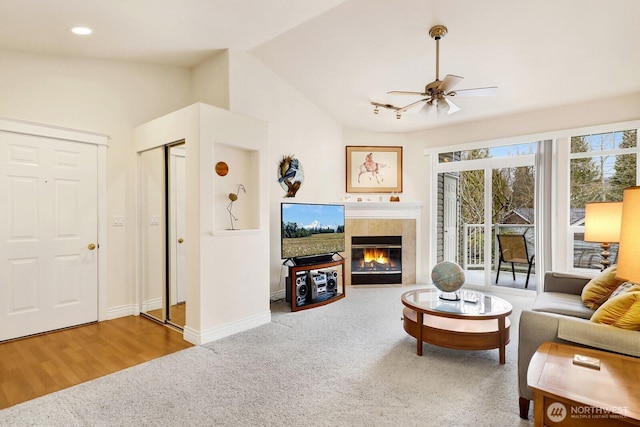 carpeted living room with baseboards, a ceiling fan, a tile fireplace, lofted ceiling, and wood finished floors