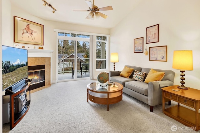 living area with rail lighting, a tiled fireplace, a ceiling fan, light carpet, and vaulted ceiling