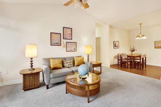 living area featuring vaulted ceiling, ceiling fan with notable chandelier, carpet flooring, and baseboards