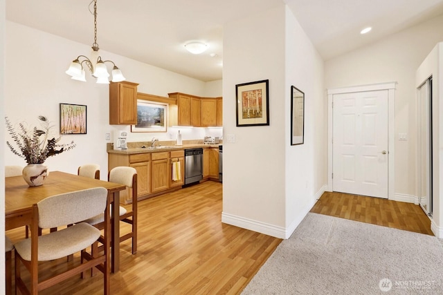 kitchen featuring light wood-style flooring, light countertops, stainless steel dishwasher, pendant lighting, and a sink