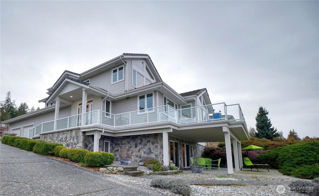 view of front of home featuring a garage, driveway, a balcony, stone siding, and a carport