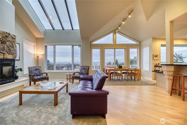 living area featuring light wood finished floors, baseboards, a fireplace, high vaulted ceiling, and track lighting