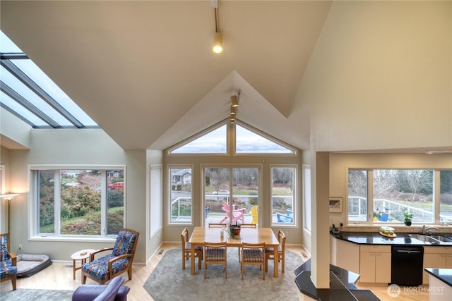 dining space featuring baseboards, lofted ceiling with skylight, light wood-type flooring, and a healthy amount of sunlight