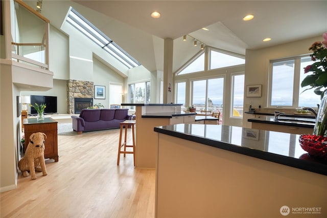 kitchen featuring a skylight, light wood-style flooring, open floor plan, a kitchen breakfast bar, and a stone fireplace