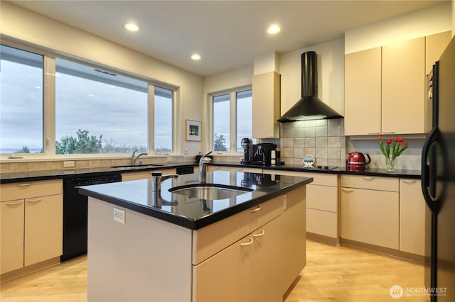 kitchen with a sink, black appliances, wall chimney exhaust hood, an island with sink, and dark countertops