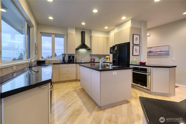 kitchen with oven, a kitchen island, wall chimney range hood, black refrigerator with ice dispenser, and dark countertops