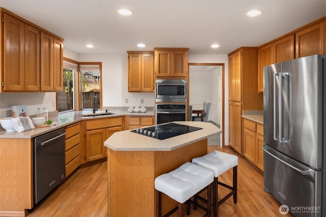 kitchen with light countertops, appliances with stainless steel finishes, a sink, a kitchen island, and a kitchen breakfast bar