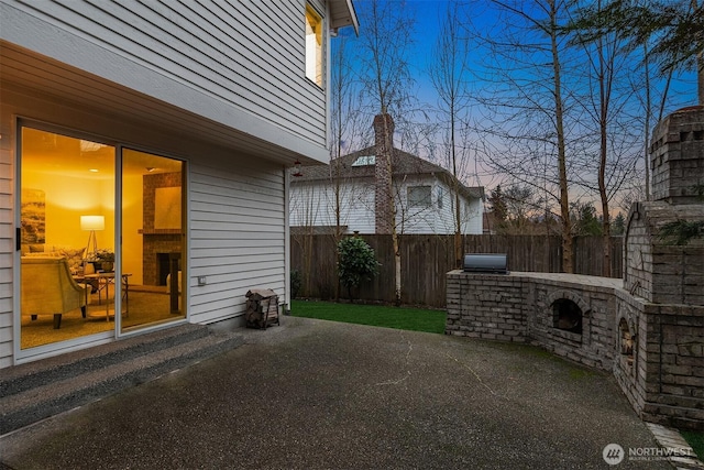 yard at dusk featuring a patio, a fireplace, and a fenced backyard