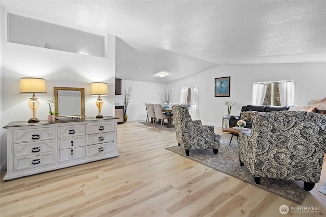 living area featuring light wood-style flooring, baseboards, vaulted ceiling, and a textured ceiling