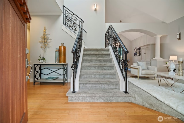 stairway featuring arched walkways, wood finished floors, baseboards, ornamental molding, and ornate columns