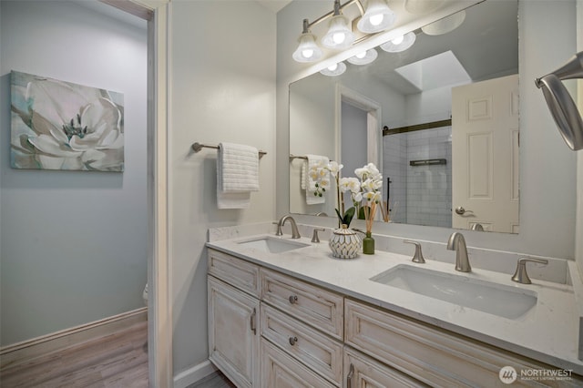 full bath featuring a skylight, a shower with shower door, a sink, and double vanity