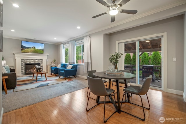 dining space featuring a stone fireplace, recessed lighting, baseboards, light wood finished floors, and crown molding