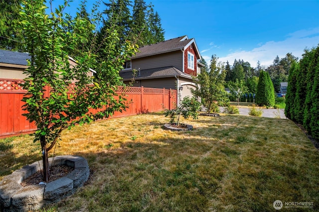 view of yard featuring a garage, an outdoor fire pit, and a fenced backyard