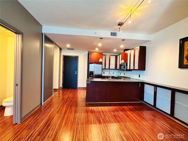 kitchen featuring glass insert cabinets, wood finished floors, a peninsula, stainless steel appliances, and a sink