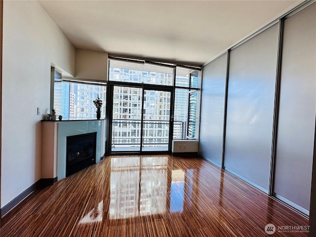 spare room with a tile fireplace, baseboards, expansive windows, and wood finished floors