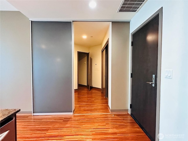 corridor with baseboards, visible vents, and light wood-style floors