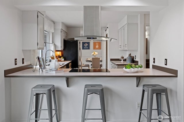 kitchen with a peninsula, white cabinetry, island range hood, and a breakfast bar area