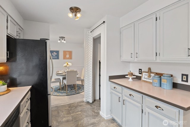 kitchen with black dishwasher, light countertops, freestanding refrigerator, and white cabinetry