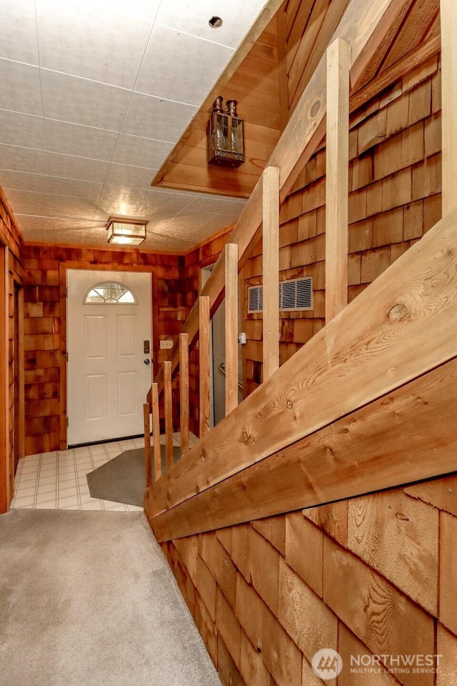 tiled entryway featuring wood walls and carpet flooring