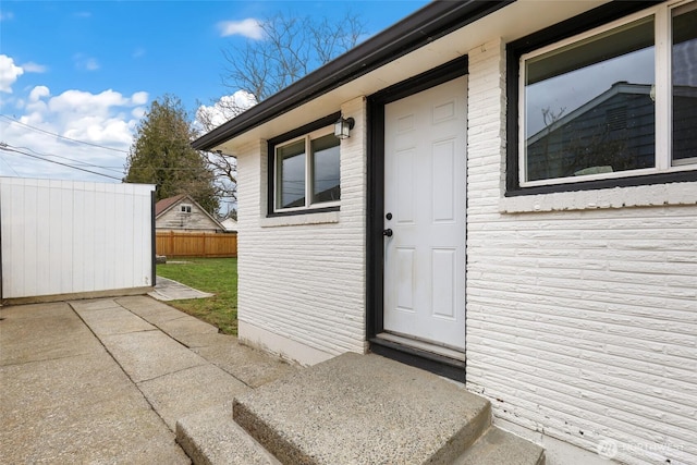 doorway to property with brick siding and fence