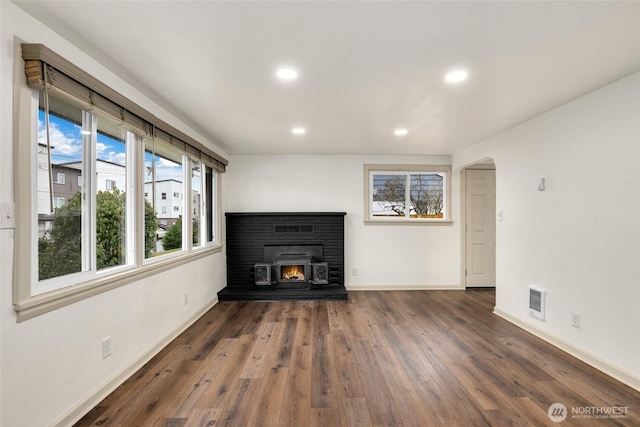 unfurnished living room featuring arched walkways, recessed lighting, wood finished floors, a lit fireplace, and baseboards