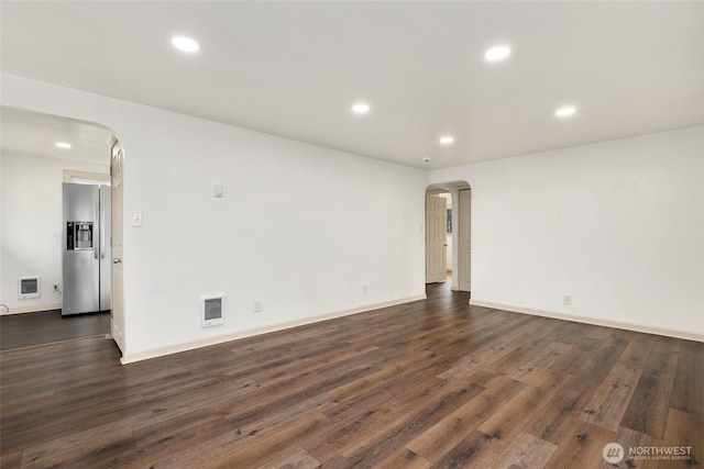 spare room featuring arched walkways, dark wood-style flooring, visible vents, and recessed lighting